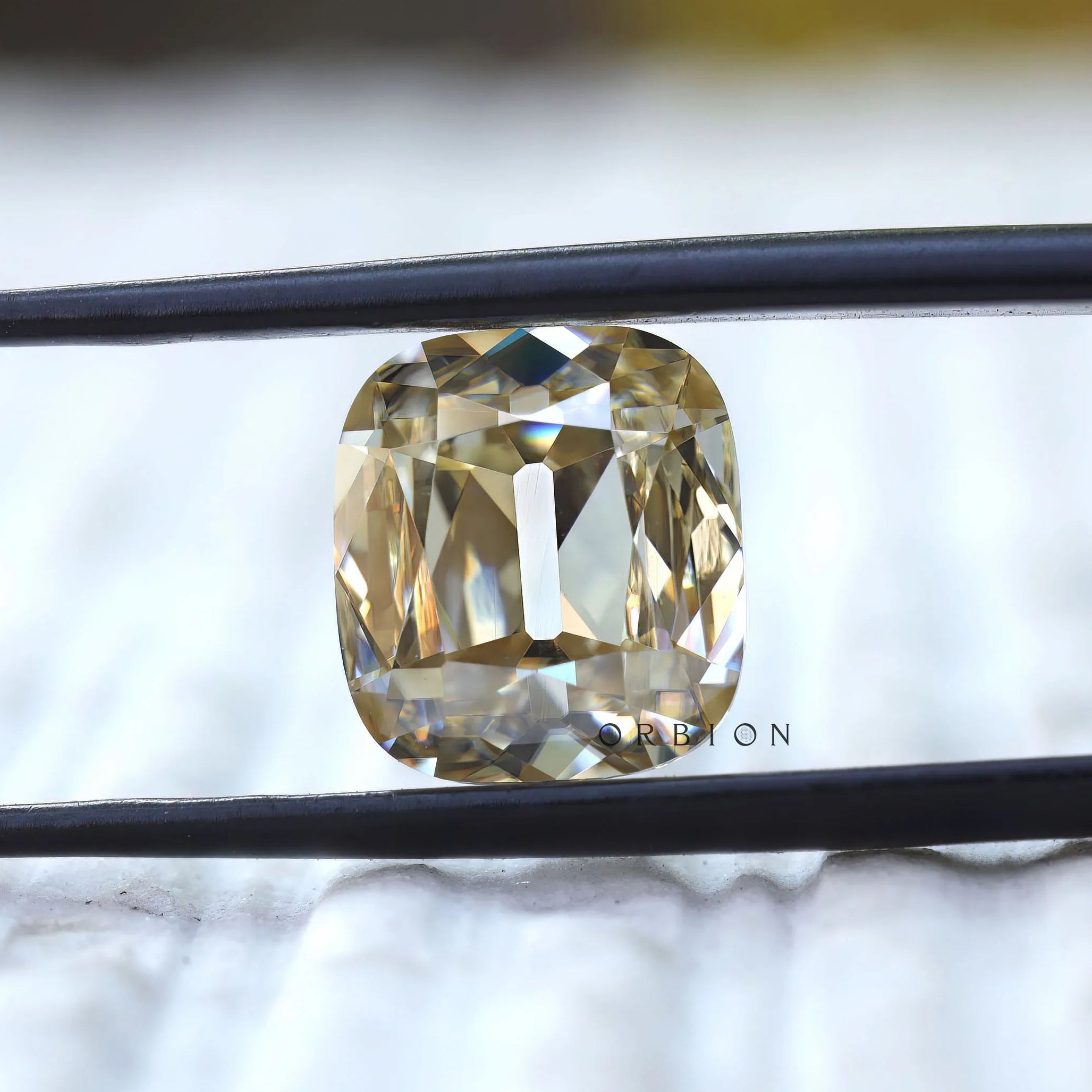 Elongated cushion old mine cut yellowish moissanite held in tweezers