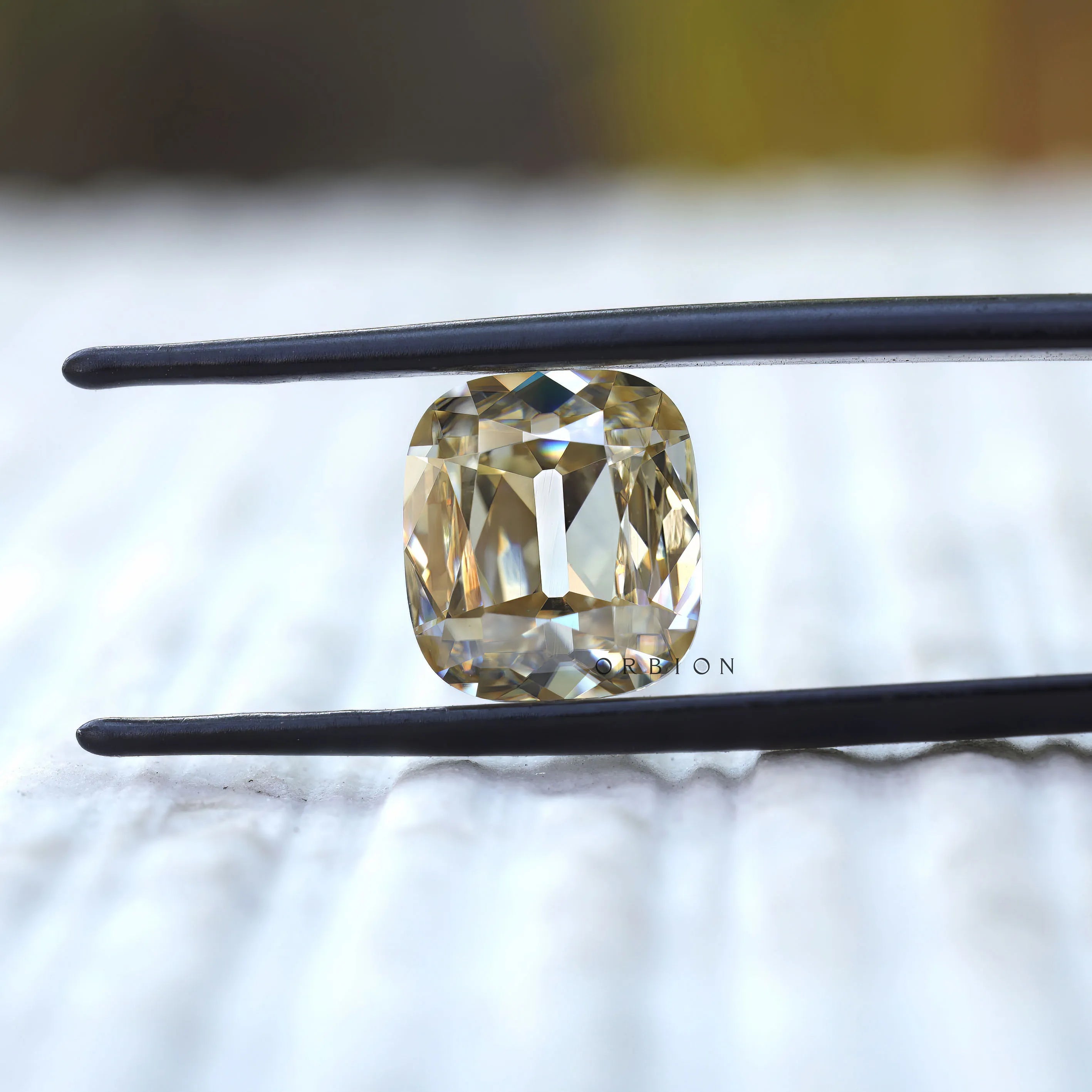 Elongated cushion old mine cut yellowish moissanite held in tweezers