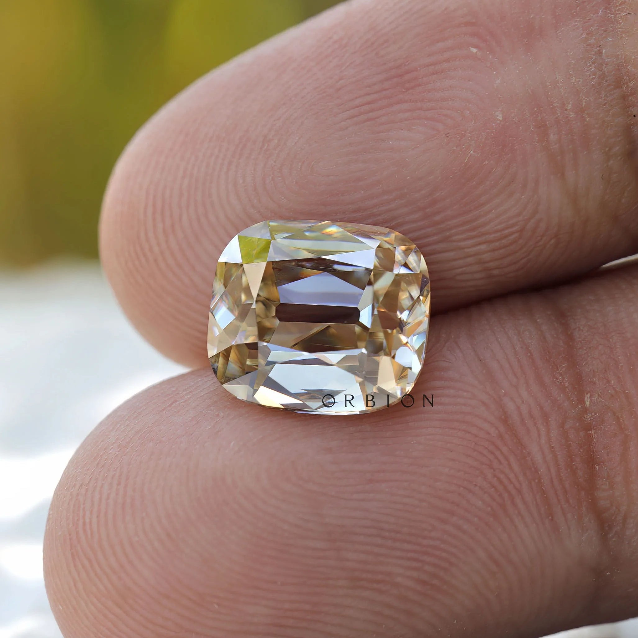 Yellowish moissanite held between fingers showing scale