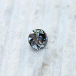 Round grey moissanite old European cut gemstone placed on textured surface