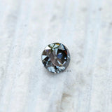 Round grey moissanite old European cut gemstone placed on textured surface
