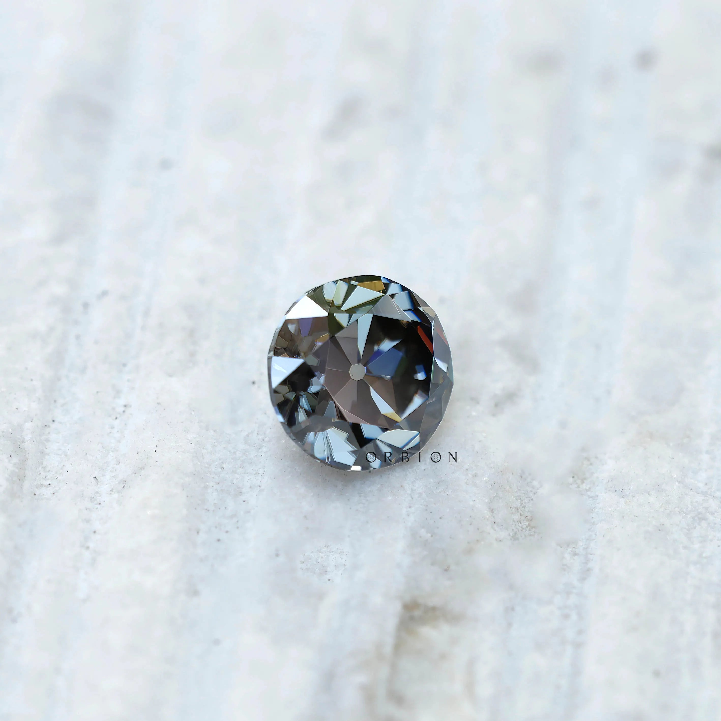 Round grey moissanite old European cut gemstone placed on textured surface