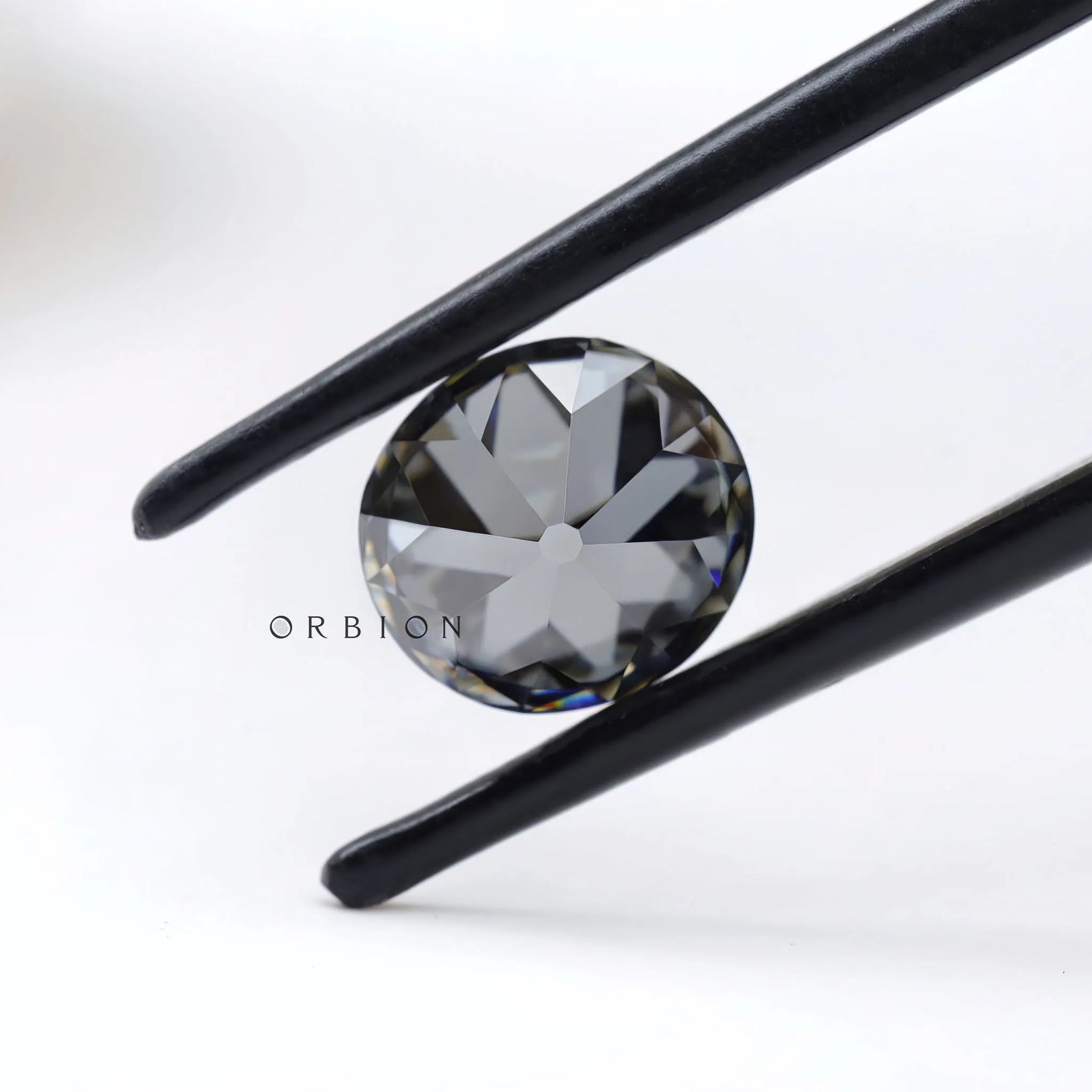 1.50 ct old european cut round dark grey moissanite loose stone, held in tweezers