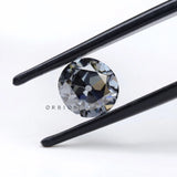 1.50 ct old european cut round dark grey moissanite loose stone, face up in tweezers