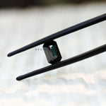 Black green moissanite emerald cut held in tweezers