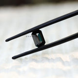 Black green moissanite emerald cut held in tweezers