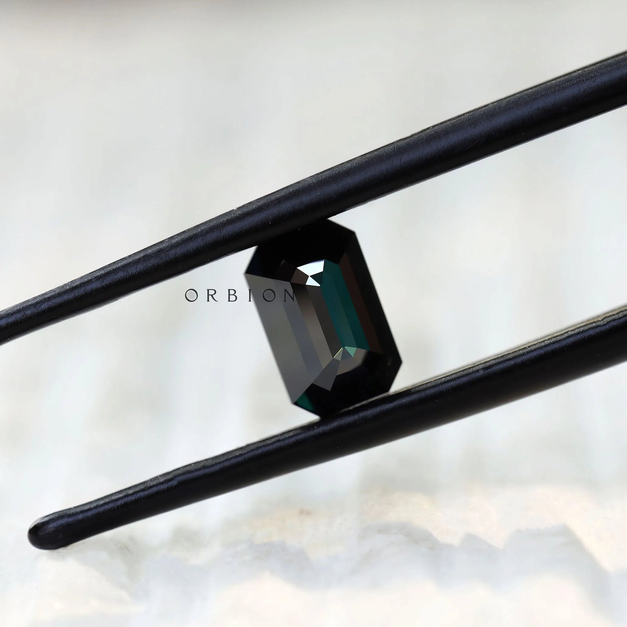 Black green moissanite emerald cut held in tweezers