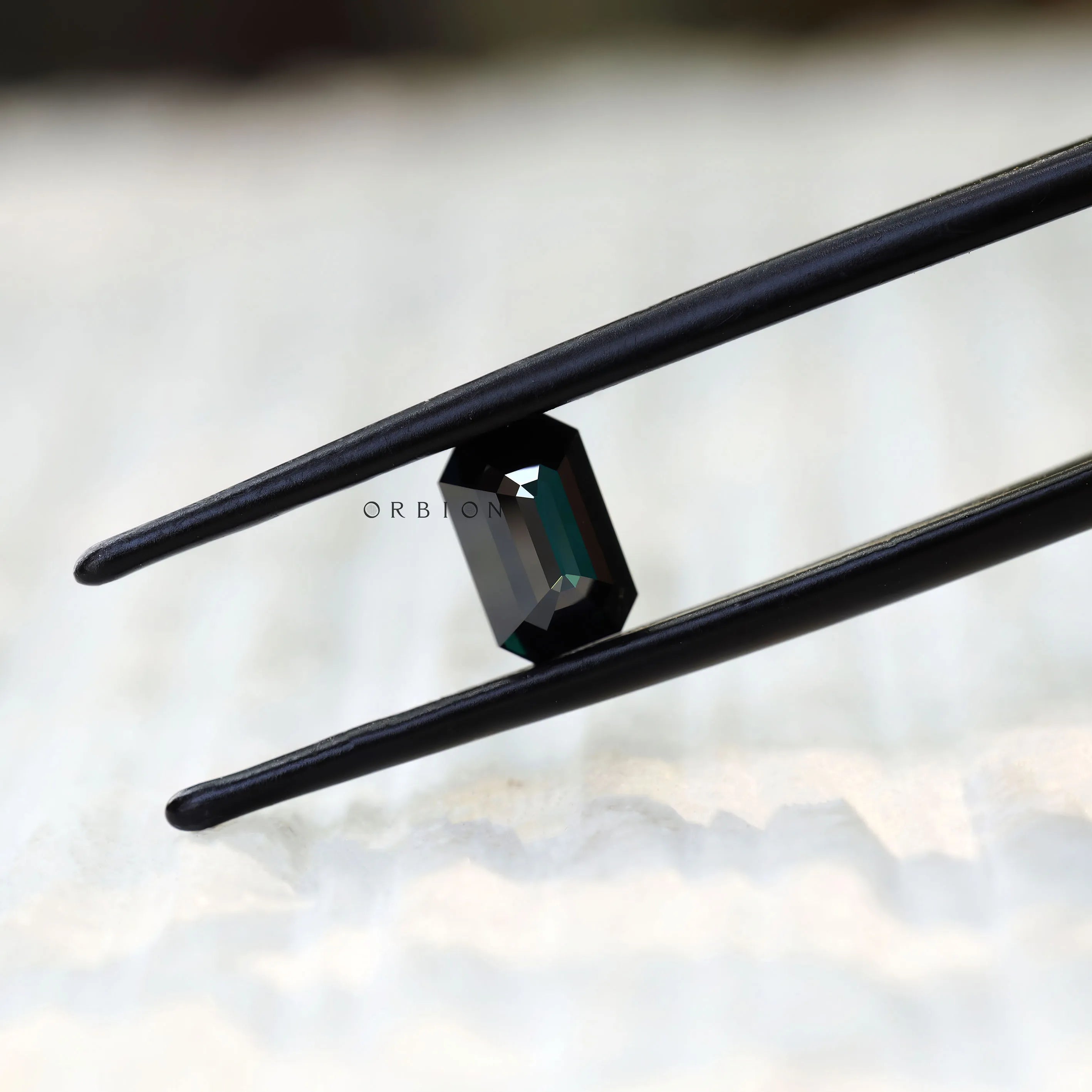 Black green moissanite emerald cut held in tweezers