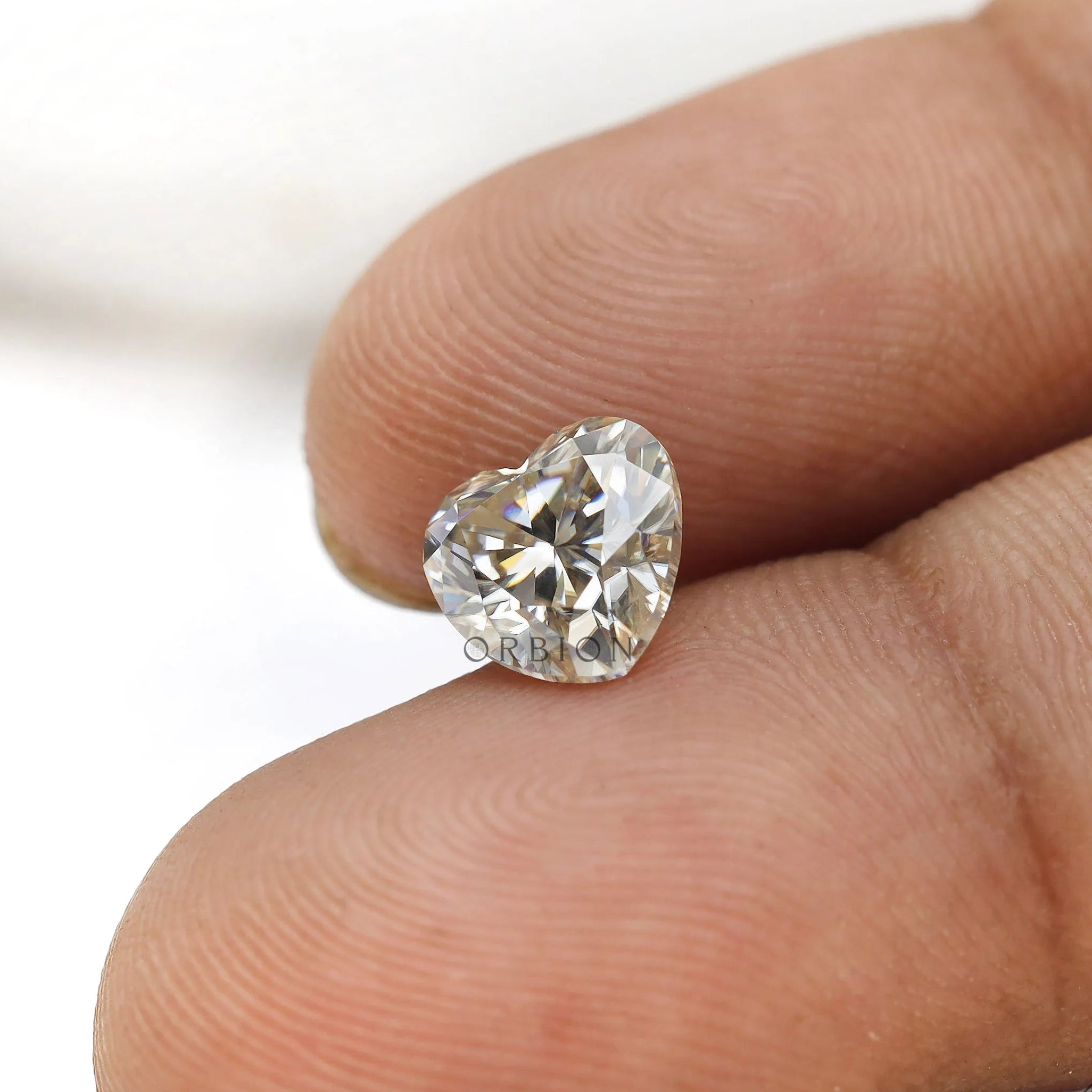 1.50 ct heart shape GHI moissanite loose stone, held on a fingertip