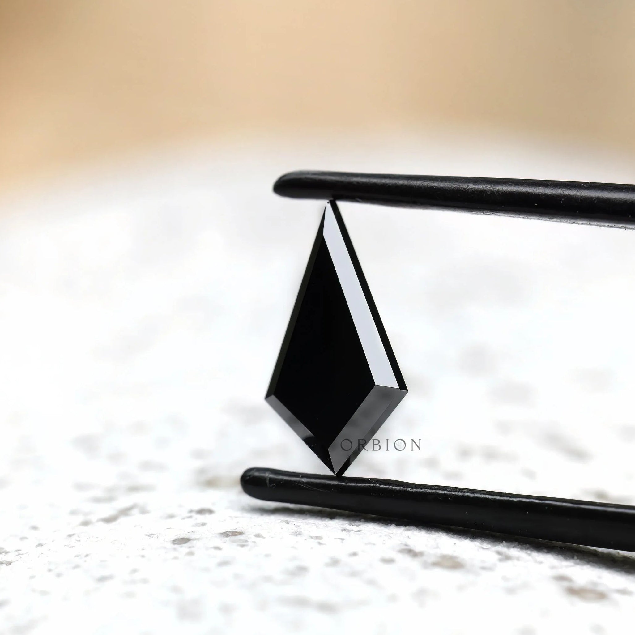 Kite cut black moissanite held in tweezers side angle