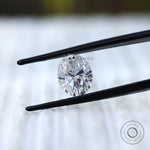 Oval moissanite gemstone held in tweezers front view