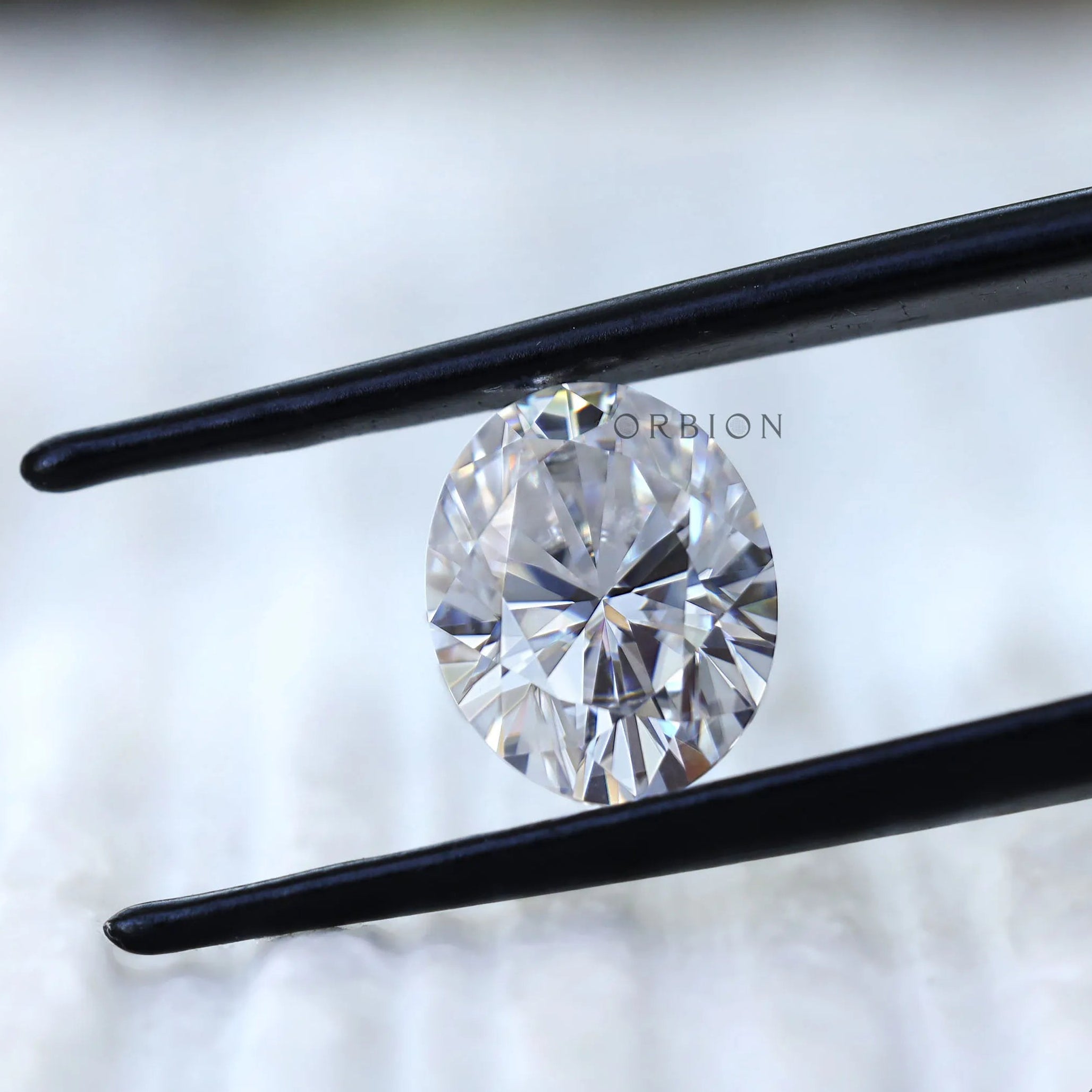 Oval moissanite gemstone held in tweezers front view