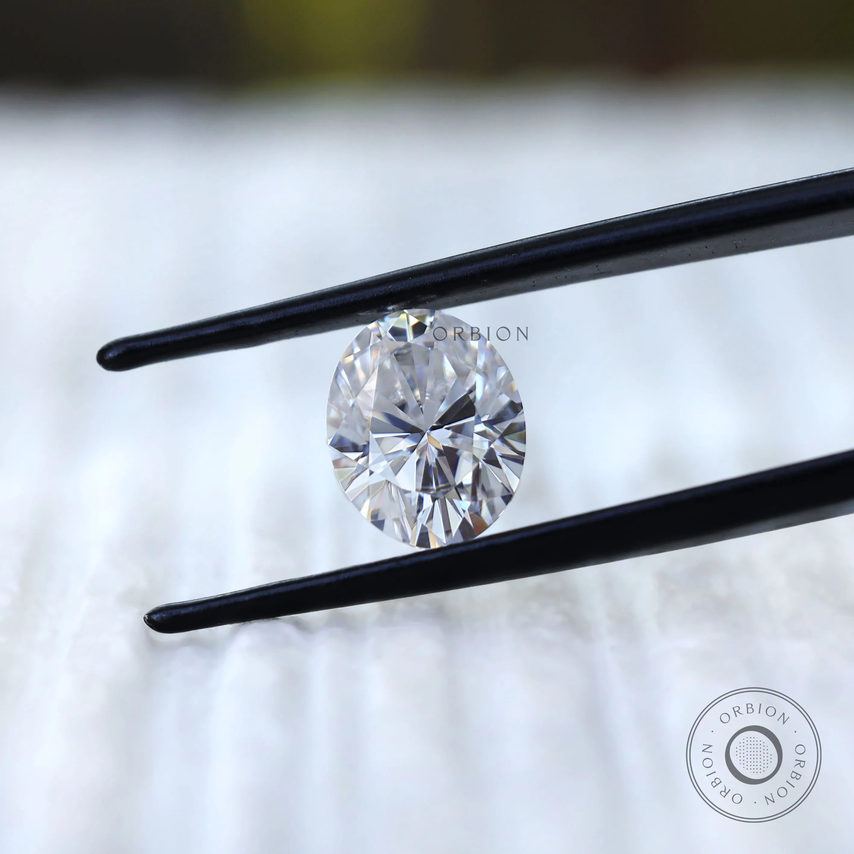 Oval moissanite gemstone held in tweezers front view