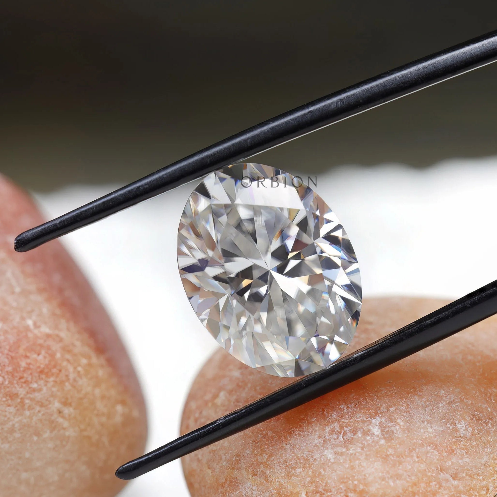 oval brilliant cut moissanite held with tweezers over stone surface