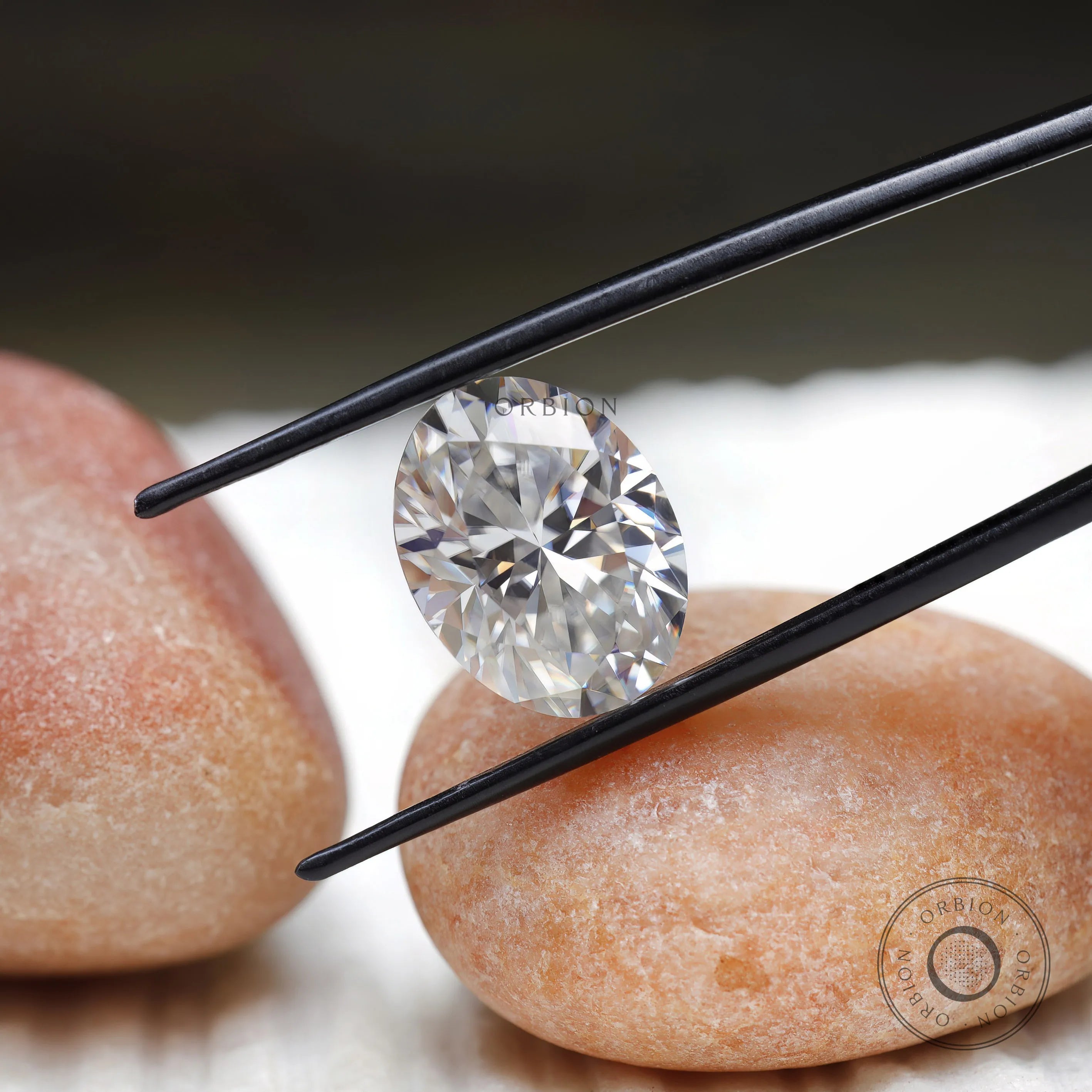 oval brilliant cut moissanite held with tweezers over stone surface