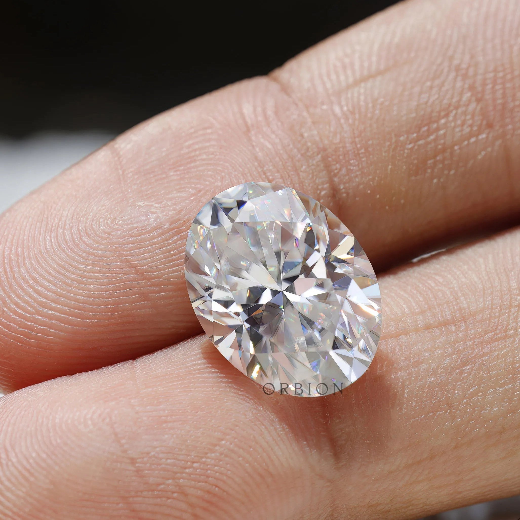 oval moissanite placed on fingertip for reference