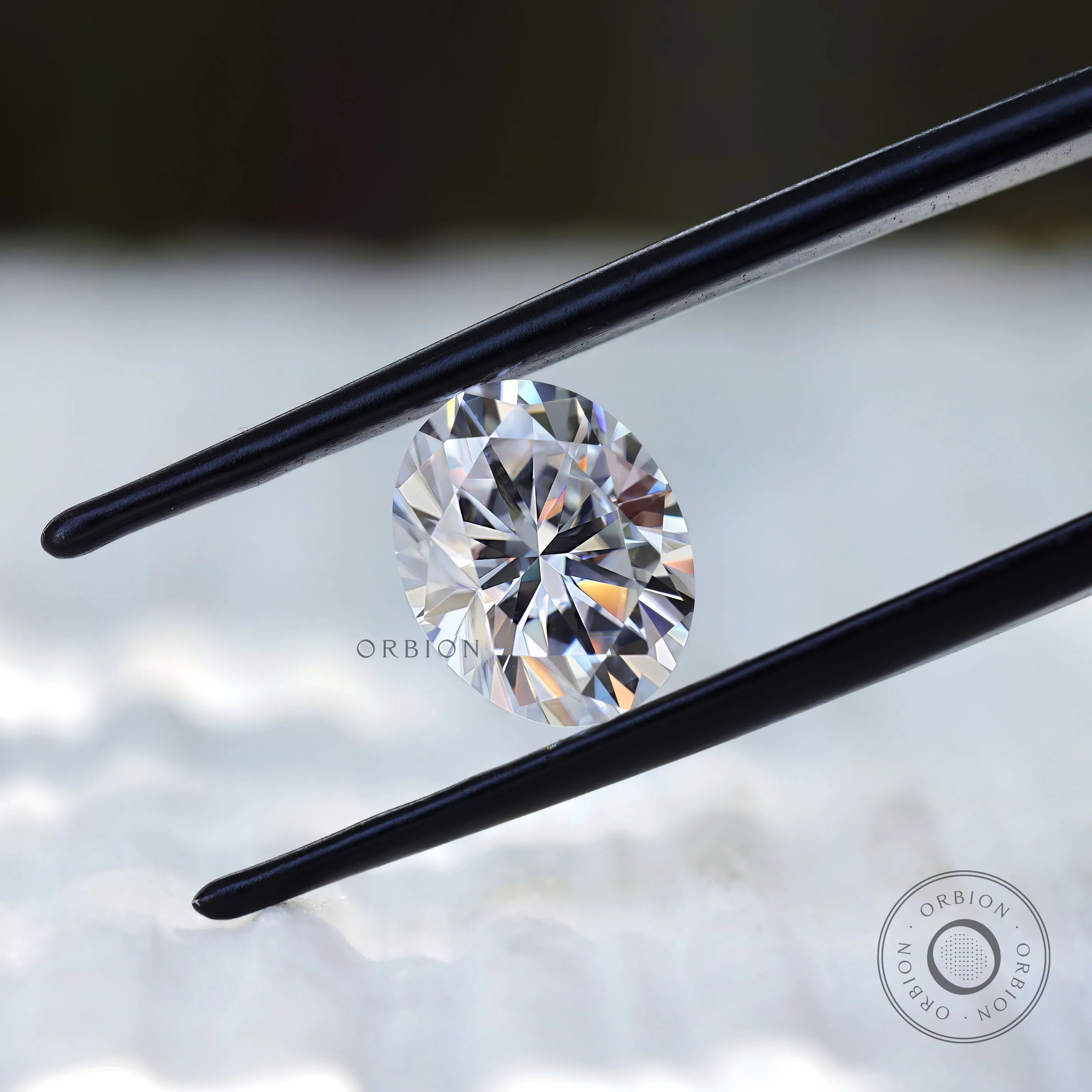 Oval moissanite gemstone held in tweezers front angle