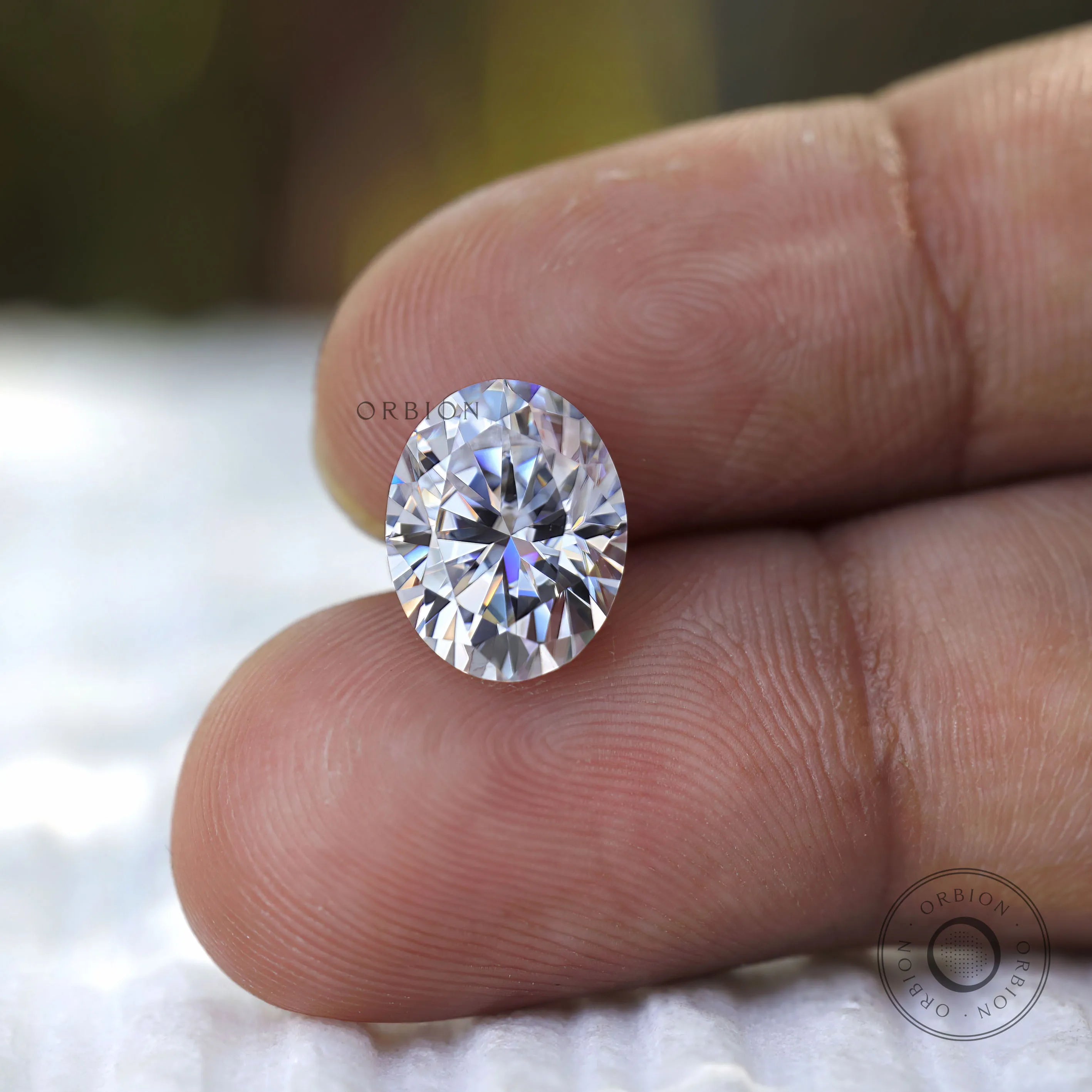 Oval cut moissanite on fingertip scale reference