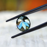 Dark green oval moissanite held in tweezers close view