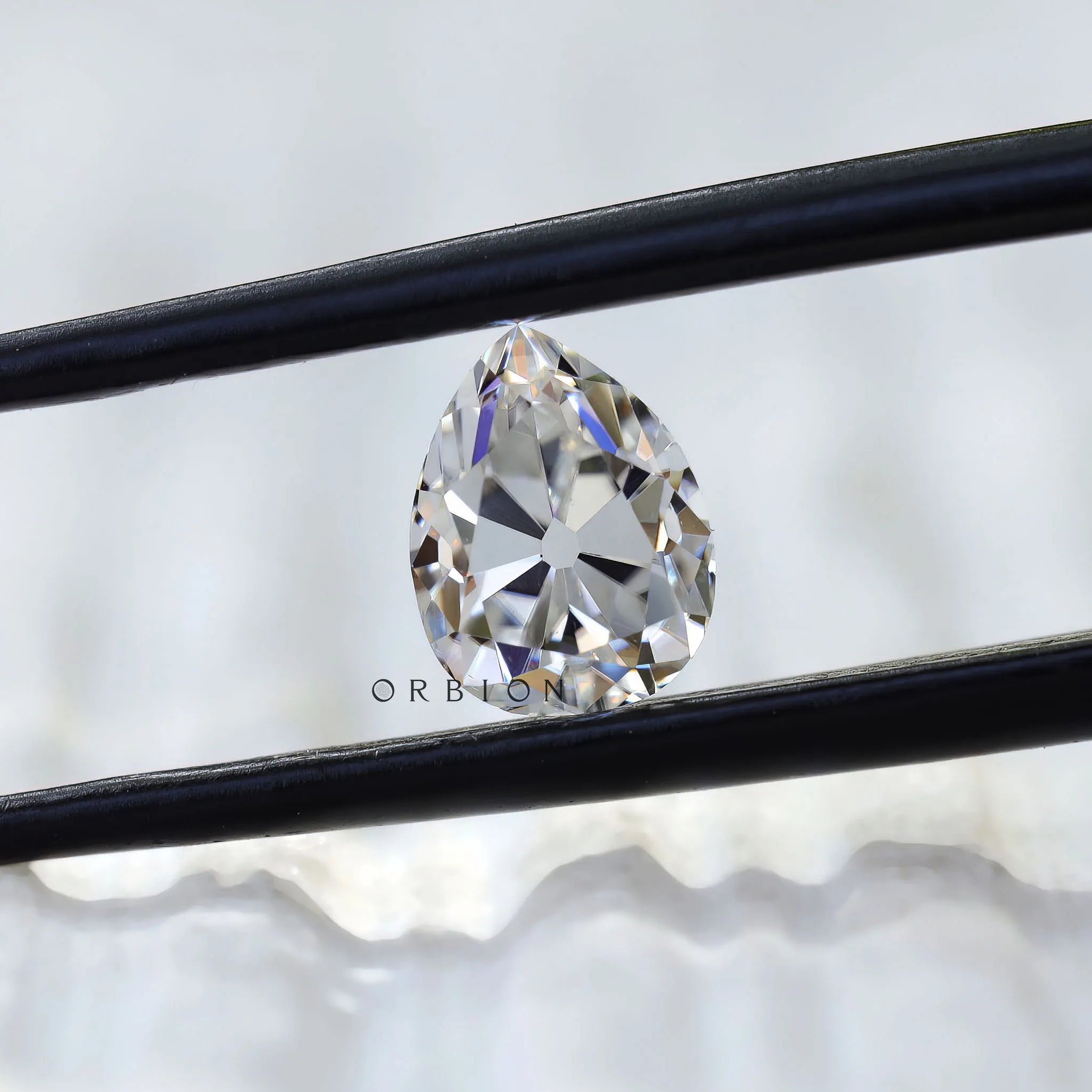 Pear old mine cut white moissanite held in tweezers