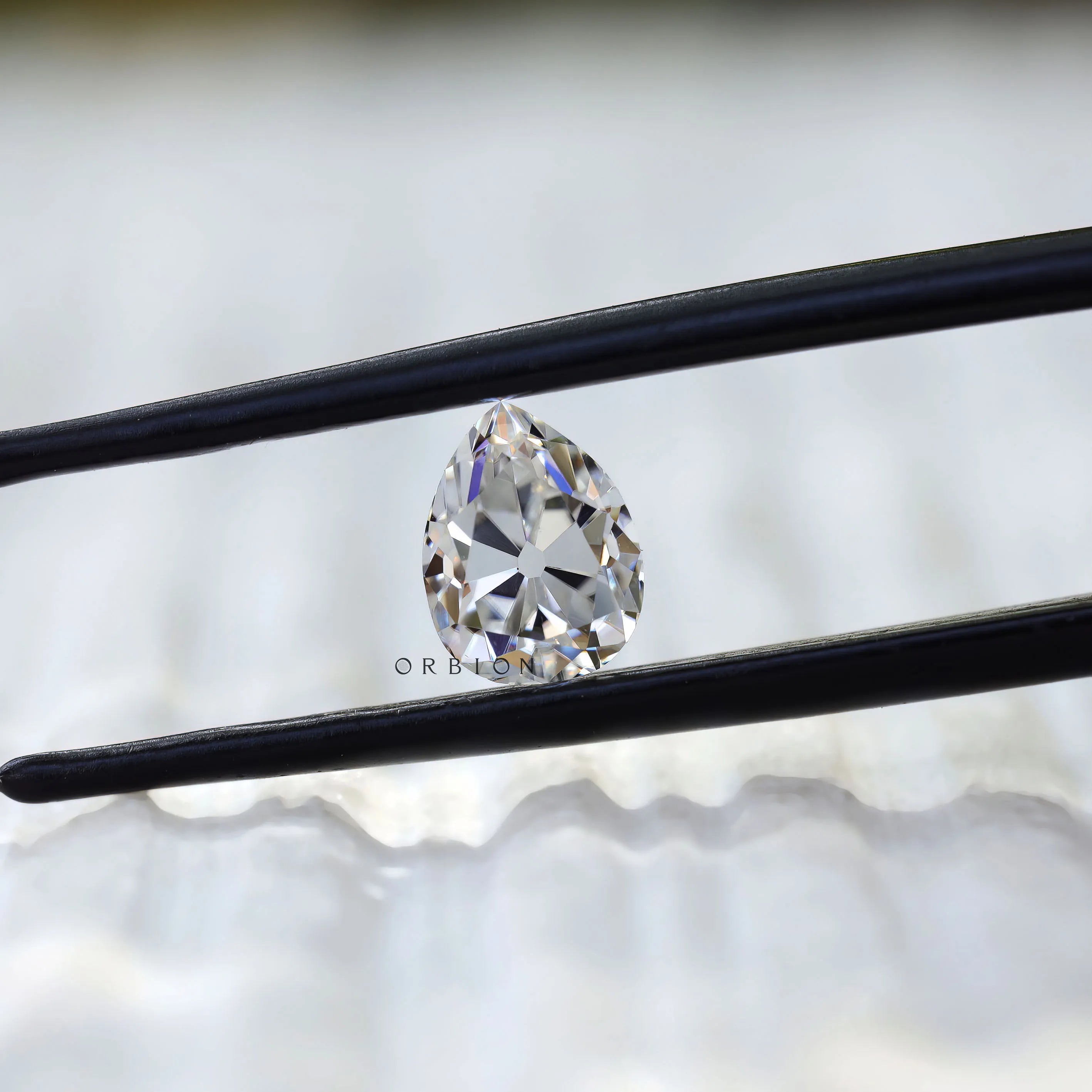 Pear old mine cut white moissanite held in tweezers