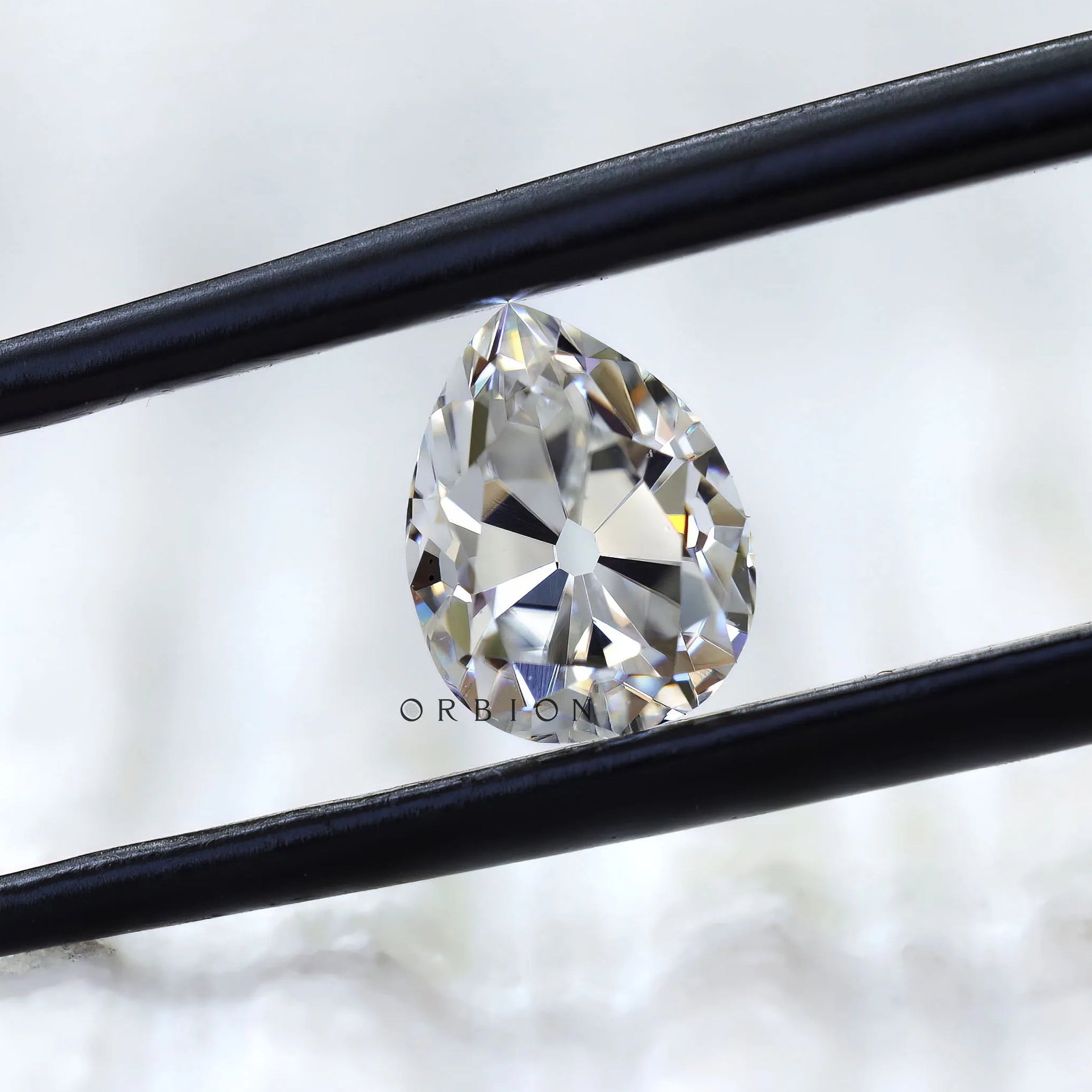 Front view of pear old mine cut moissanite in tweezers