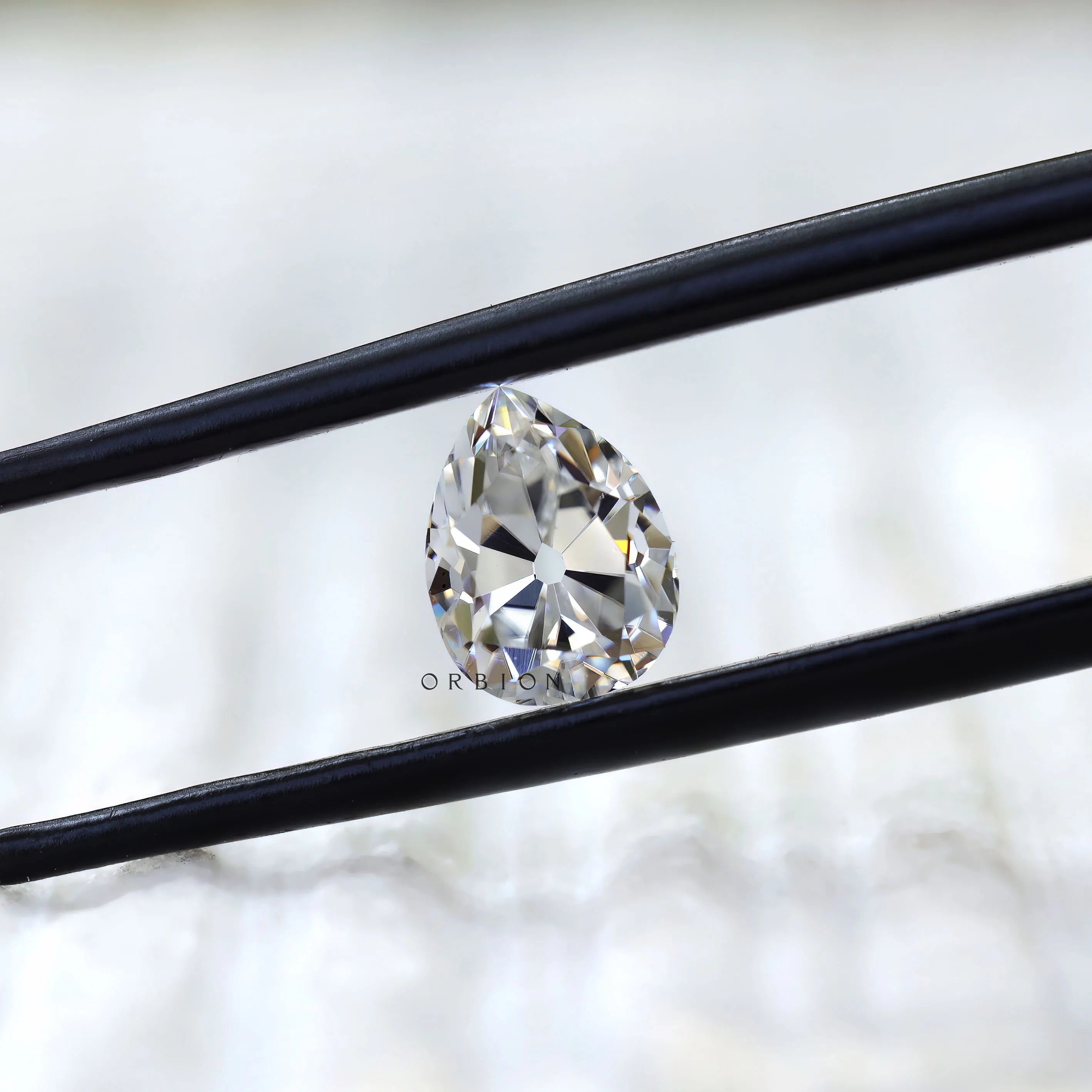Front view of pear old mine cut moissanite in tweezers