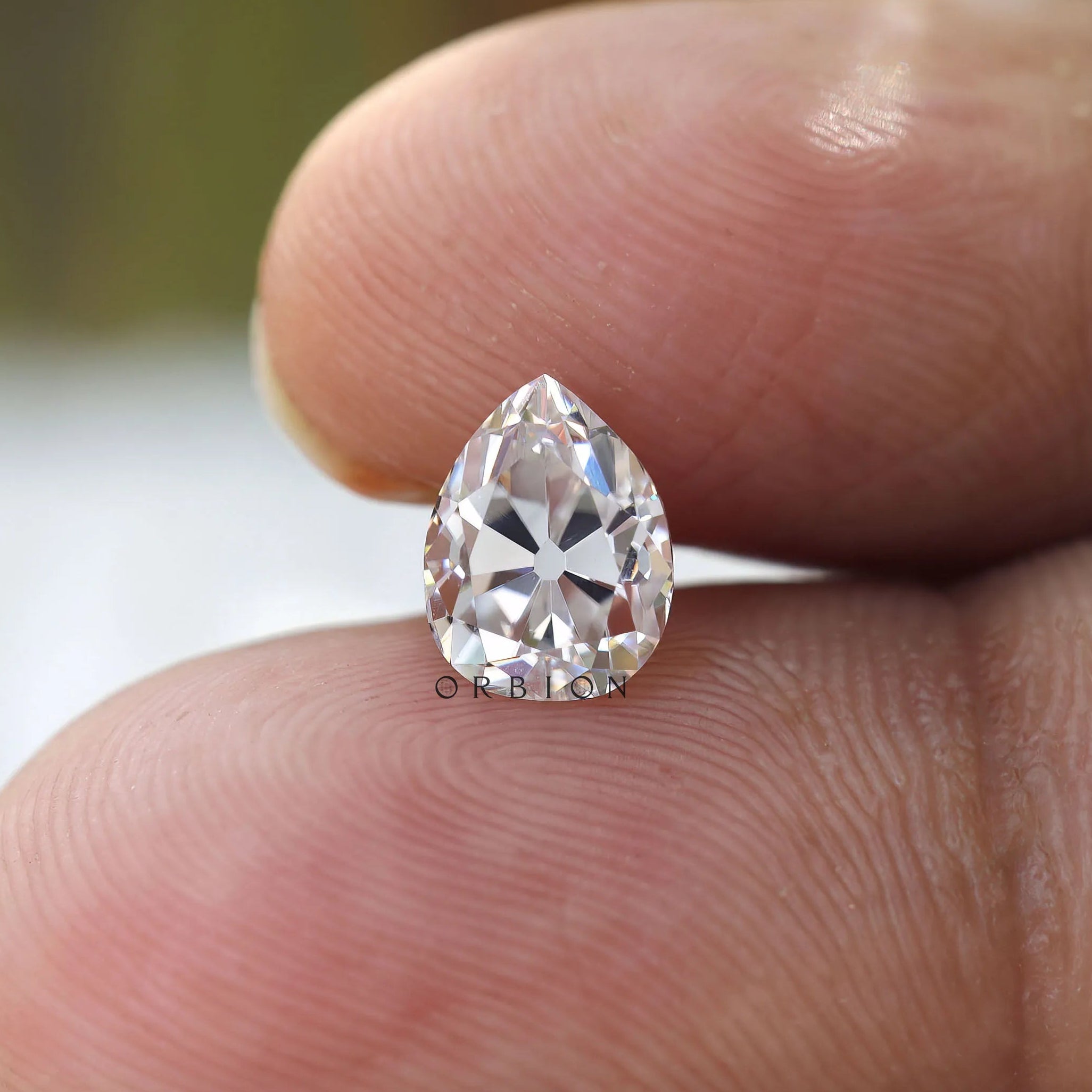 Close finger shot showing brilliance of pear moissanite