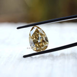Yellowish pear moissanite held in tweezers close view