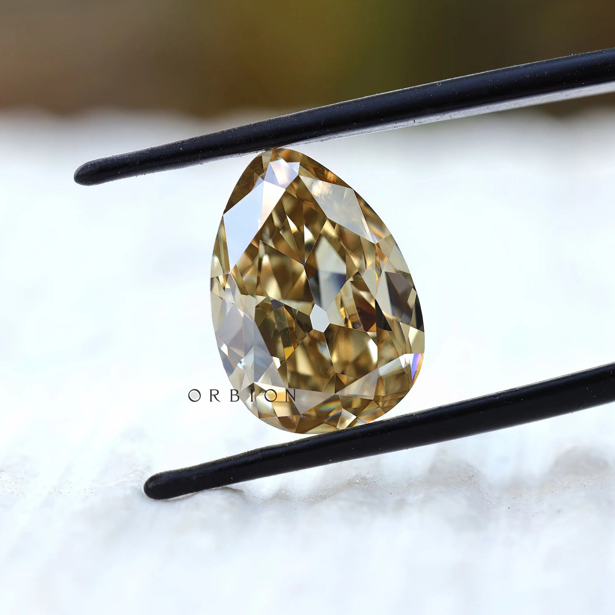 Yellowish pear moissanite held in tweezers close view