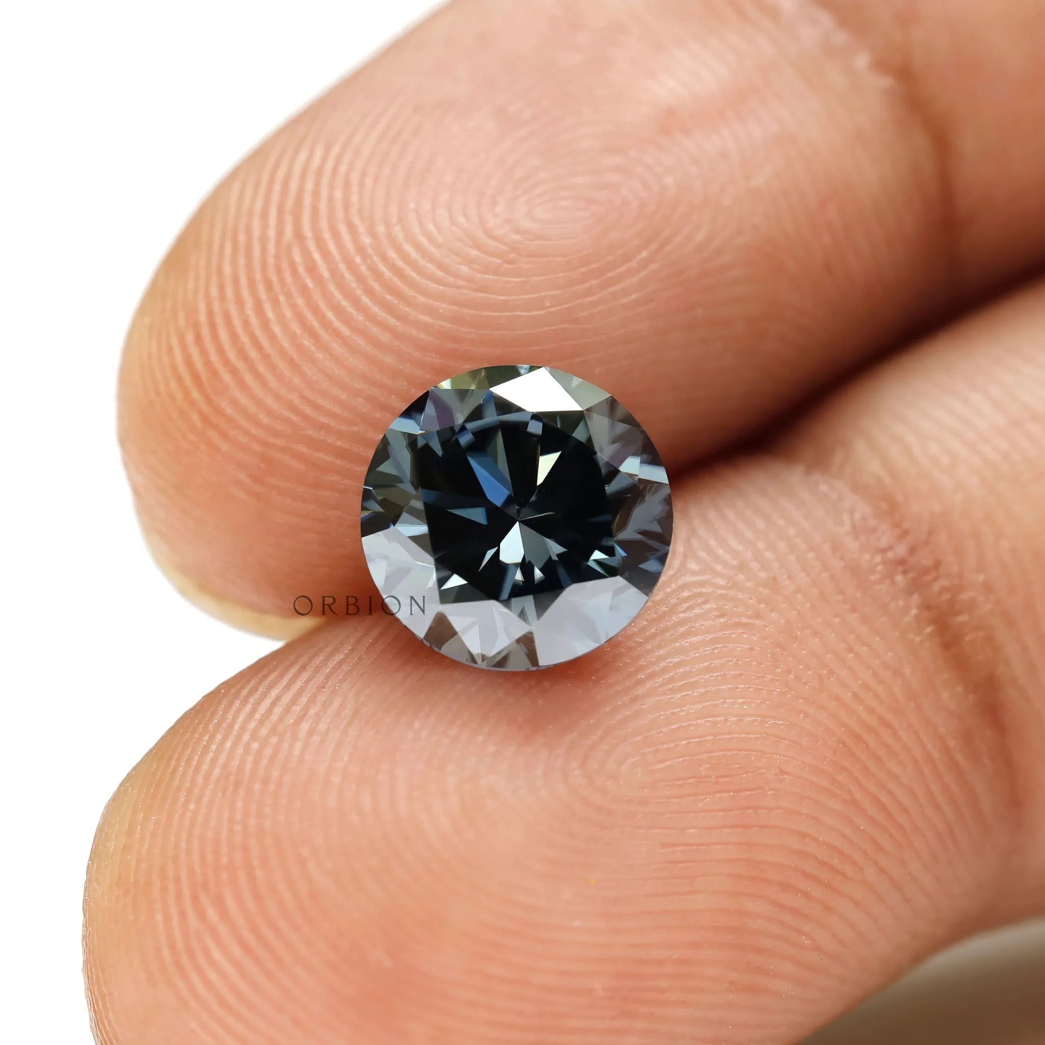 Round dark grey moissanite brilliant cut gemstone held between fingers showing sparkle