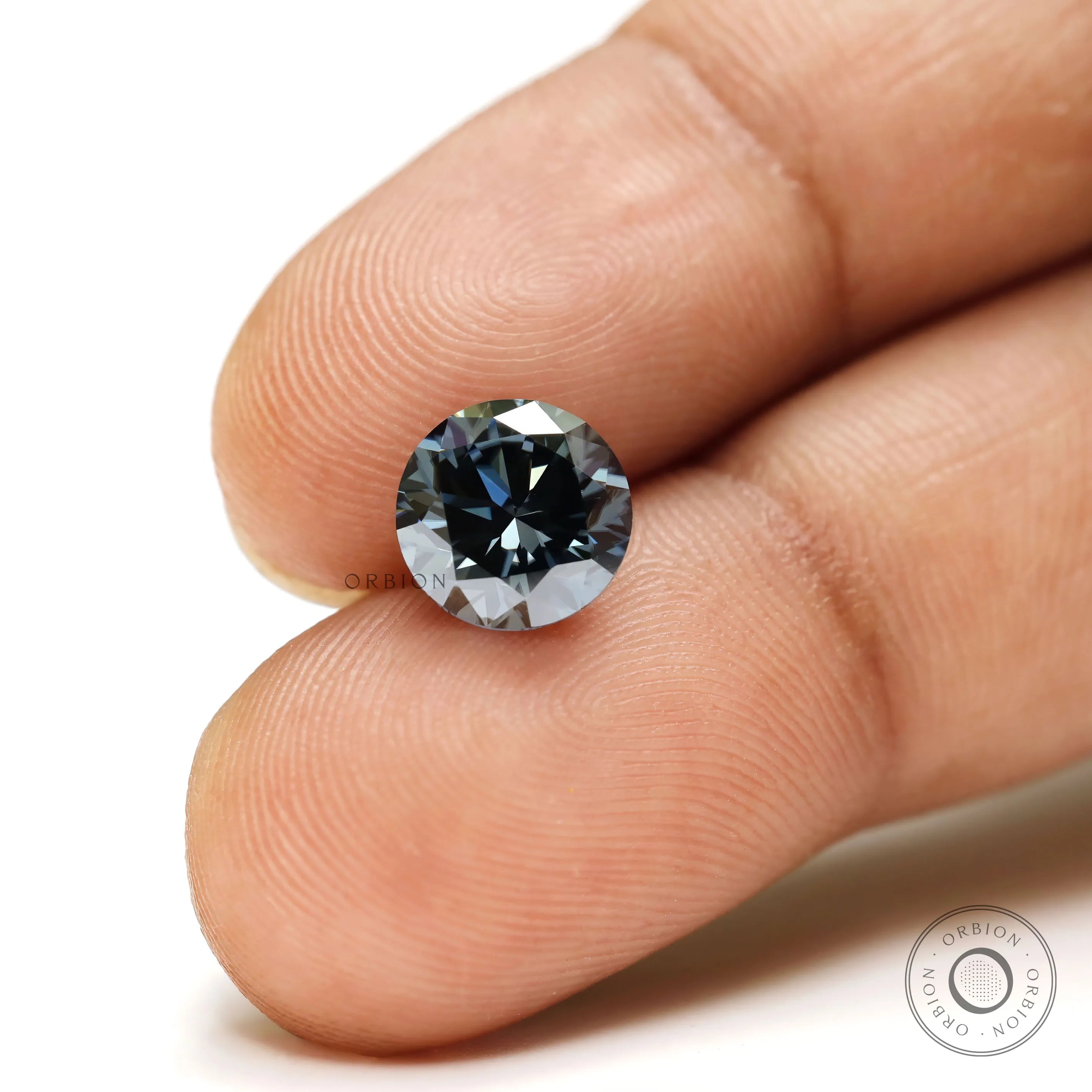 Round dark grey moissanite brilliant cut gemstone held between fingers showing sparkle