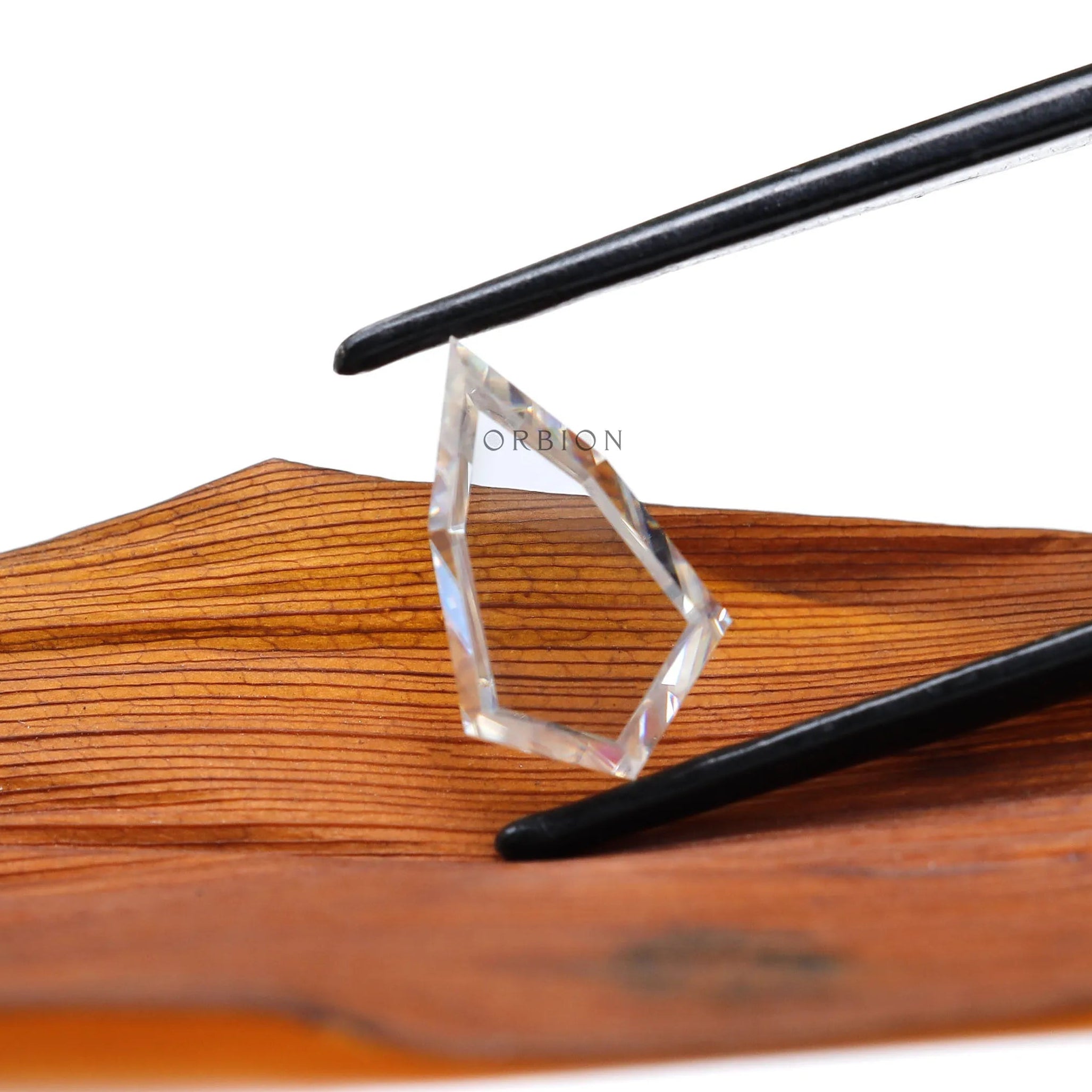 Shield portrait cut moissanite held with tweezers on wooden background