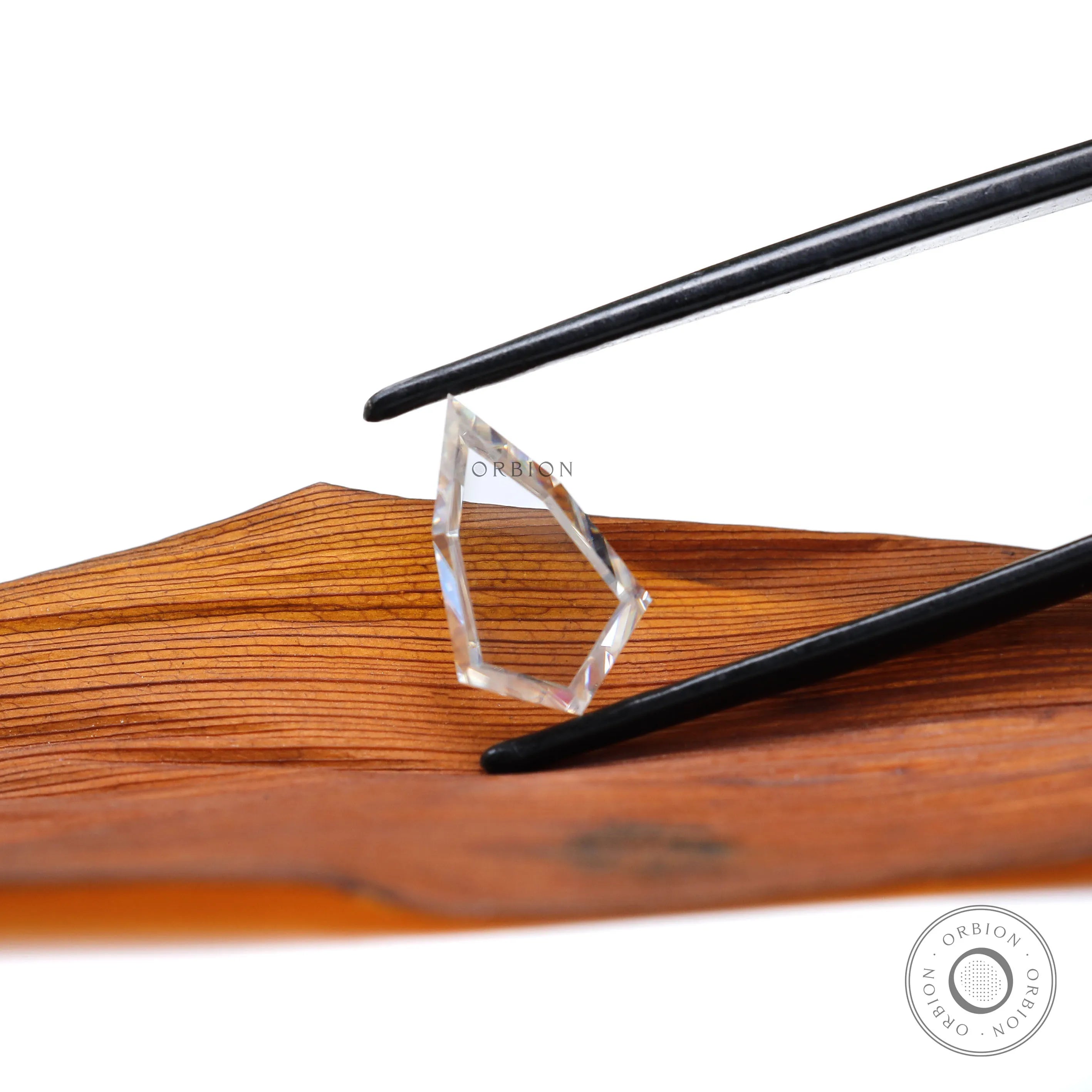 Shield portrait cut moissanite held with tweezers on wooden background