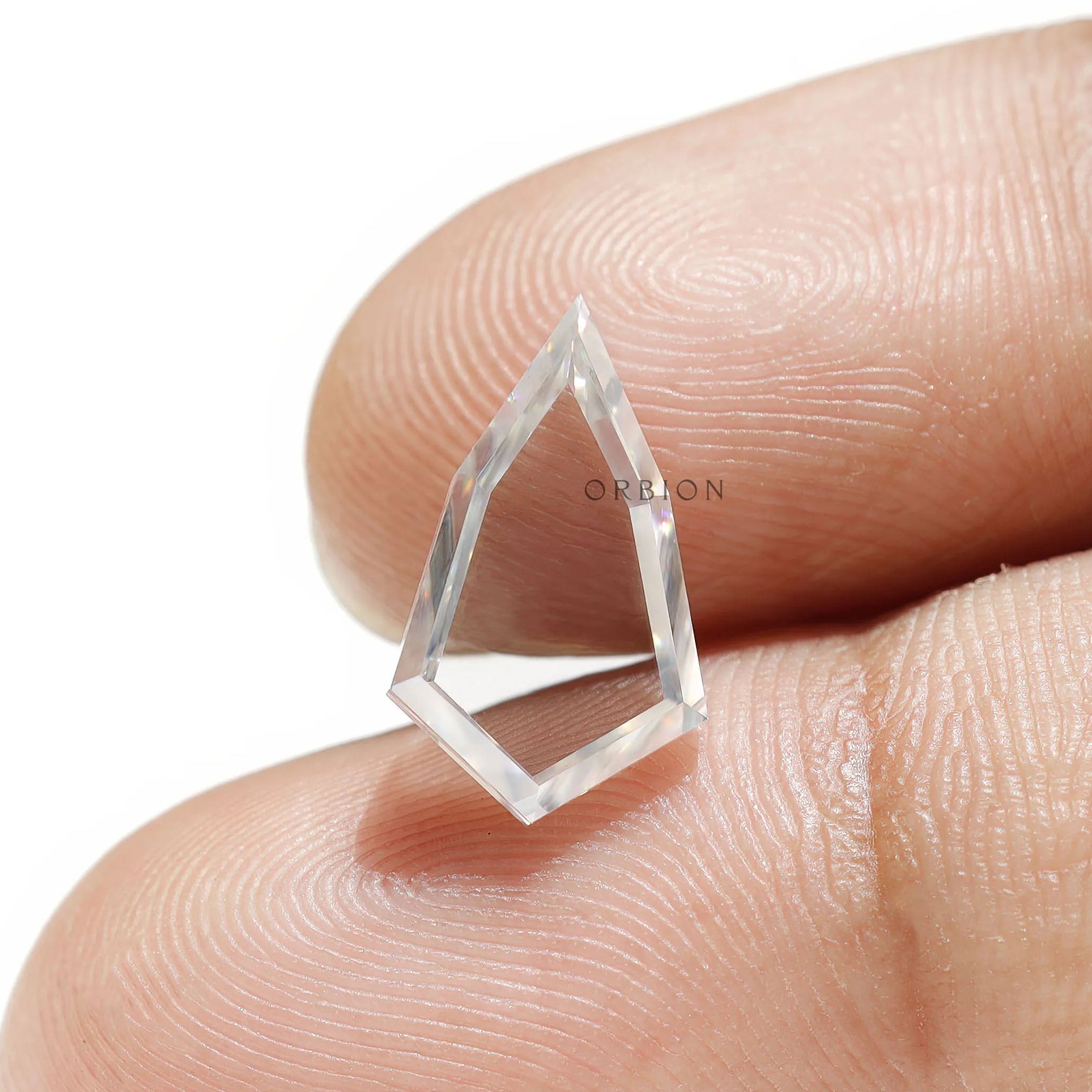 Shield shaped moissanite placed on fingertip showing transparency