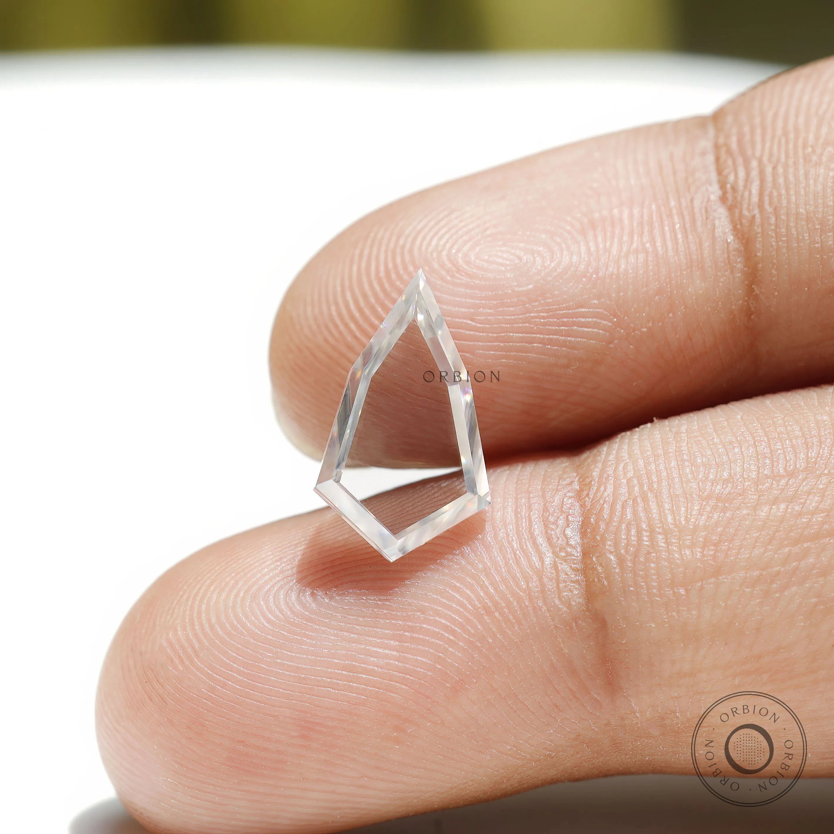 Shield shaped moissanite placed on fingertip showing transparency