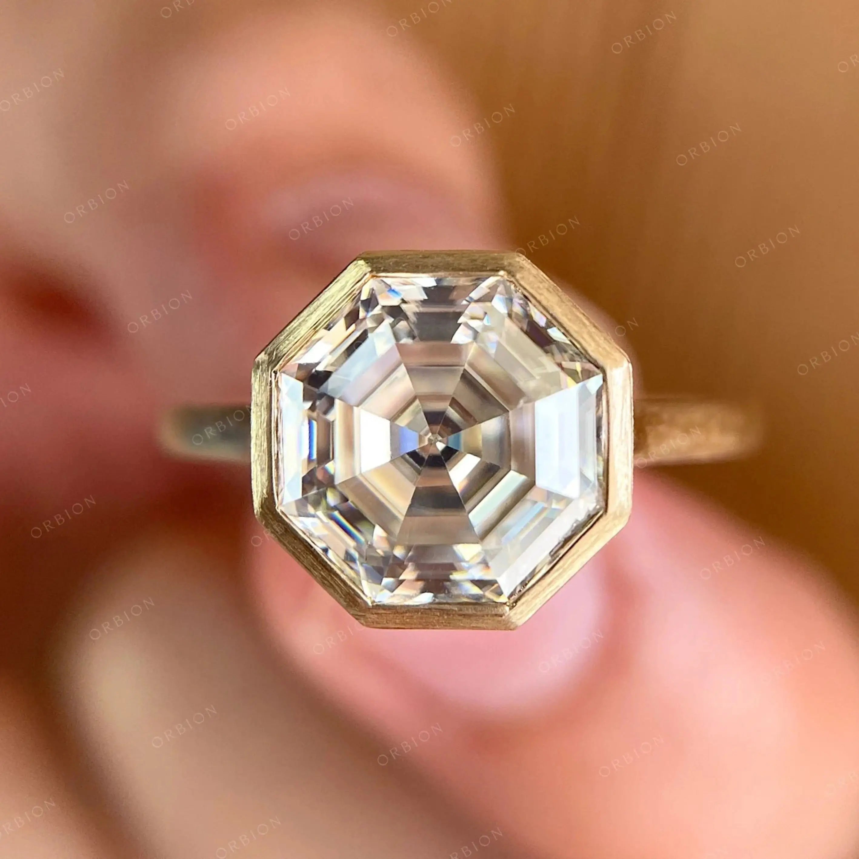 Moissanite octagon step cut bezel set cathedral style solitaire ring in 10K yellow gold.