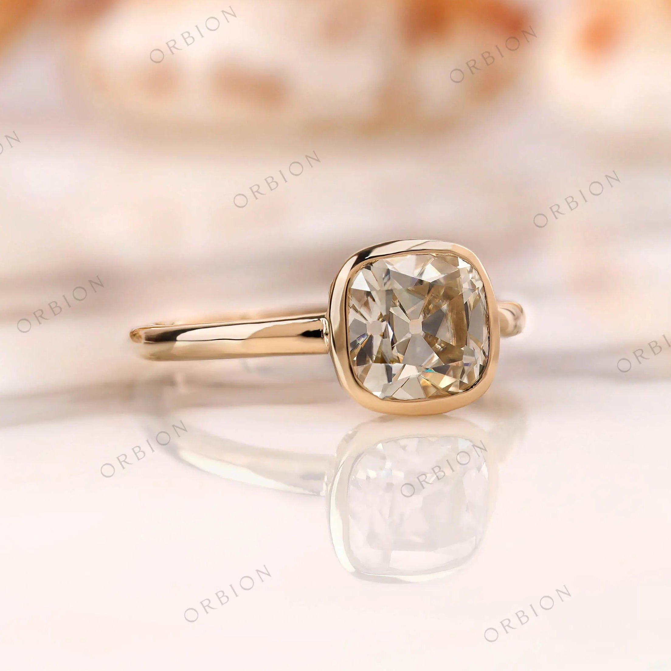 Angled view of Old Mine Cut cushion Moissanite bezel ring in yellow gold.