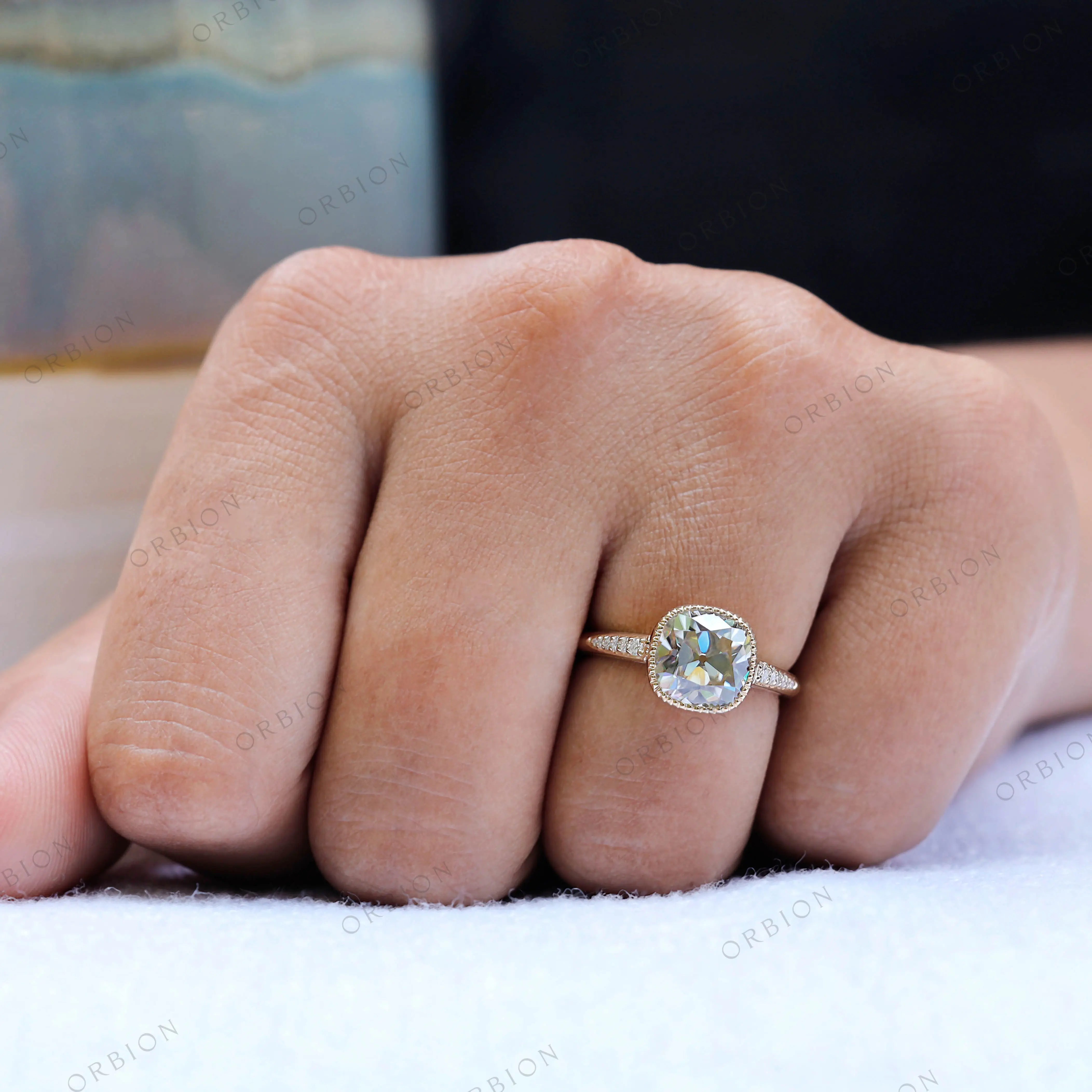 Profile view of Bezel Set Cushion Cut Moissanite Engagement Ring on a finger with delicate side stone detailing