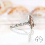 Side view of pear Moissanite halo ring with round brilliant cut side stones in white gold.