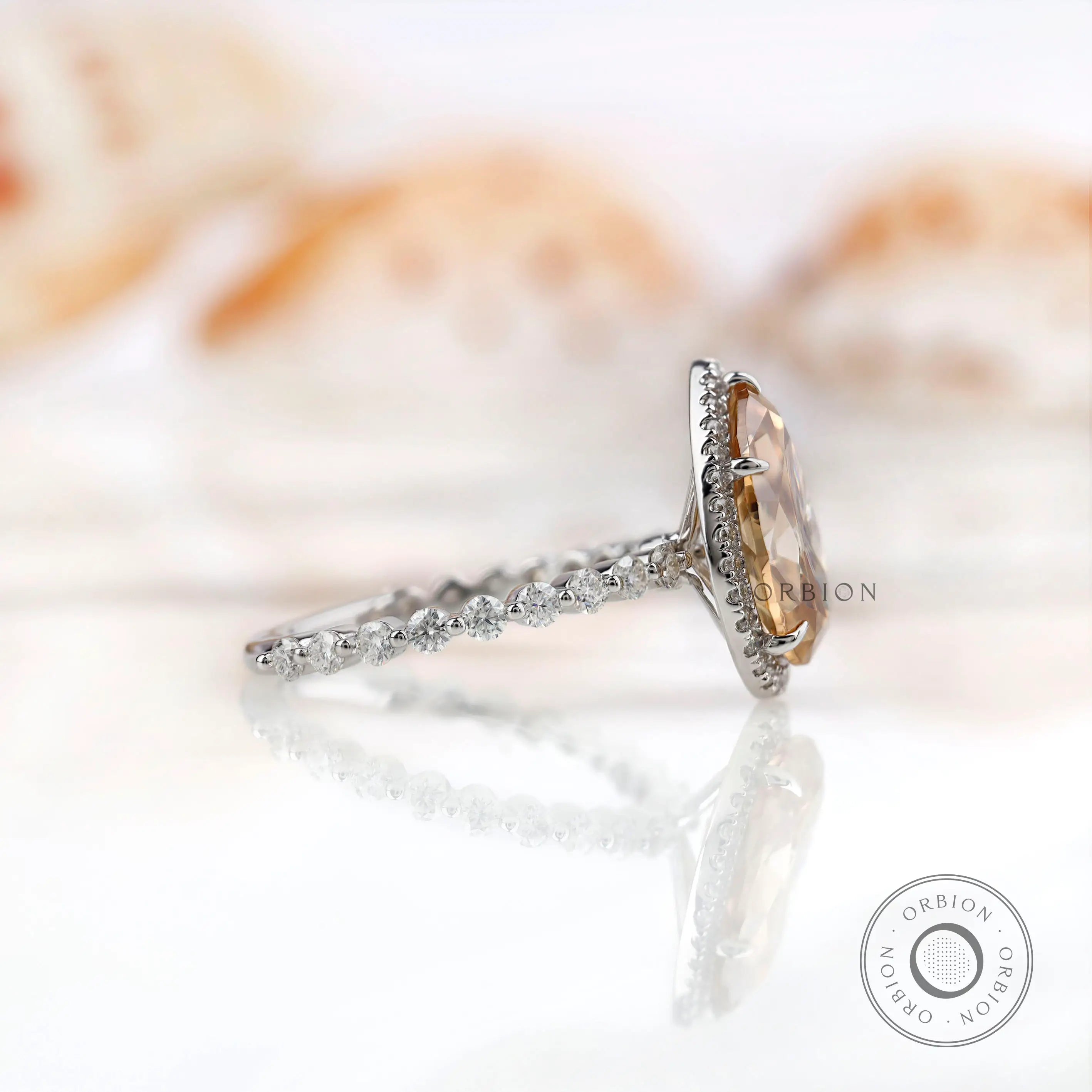 Side view of pear Moissanite halo ring with round brilliant cut side stones in white gold.