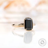 Close-up view of solitaire emerald cut black green moissanite in yellow gold