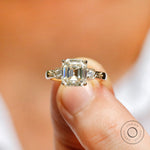 Moissanite three-stone engagement ring featuring a step-cut Asscher center stone and round Moissanite side stones in 10K yellow gold