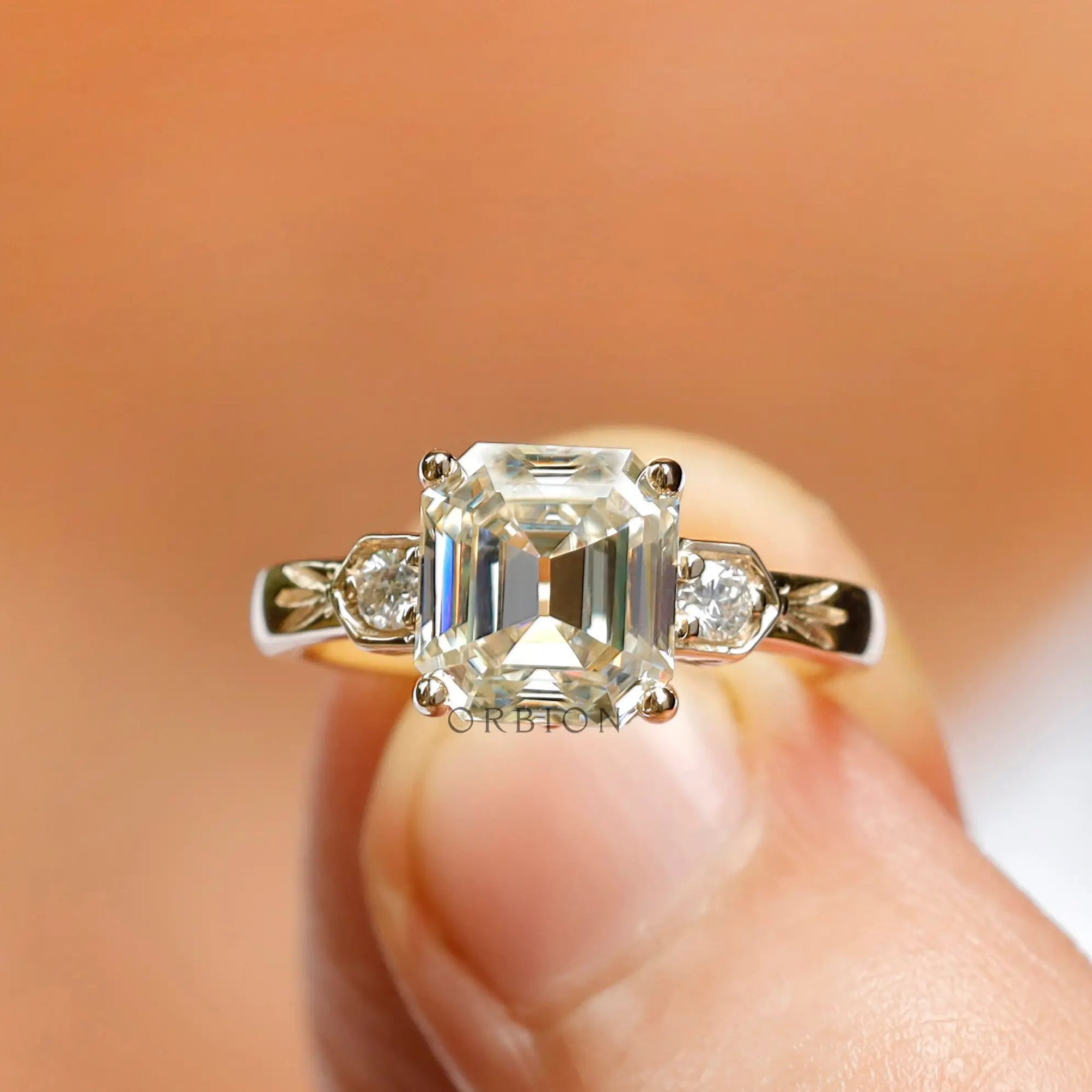 Moissanite three-stone engagement ring featuring a step-cut Asscher center stone and round Moissanite side stones in 10K yellow gold