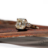 Profile shot of the three-stone engagement ring, highlighting the Asscher cut Moissanite and two round side stones in 10K yellow gold.
