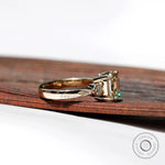 Side view of a three-stone engagement ring with a step-cut Asscher Moissanite center and two round Moissanite side stones, set in 10K yellow gold.