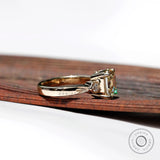 Side view of a three-stone engagement ring with a step-cut Asscher Moissanite center and two round Moissanite side stones, set in 10K yellow gold.