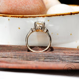 A side view of the three-stone engagement ring with a step-cut Asscher Moissanite center stone and round Moissanite side stones in 10K yellow gold.