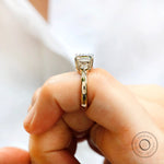 Close-up of the Asscher cut Moissanite center stone ring with two round side stones in 10K yellow gold.