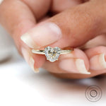 Close up side angle heart solitaire ring held against soft white background